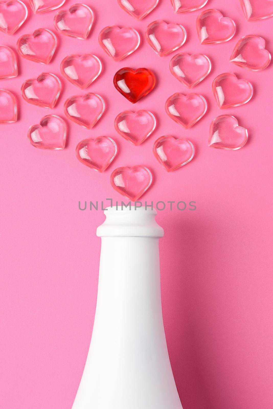 Valentines Day Concept: high angle shot of a white champagne bottle with pink glass hearts simulating a spray. by sCukrov