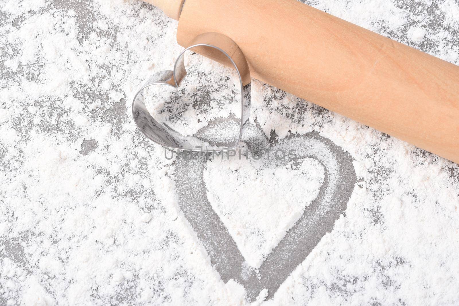 Valentines Day Concept: A heart shaped cookie cutter with flour and rolling pin and heart shape drawn in the flour. . 