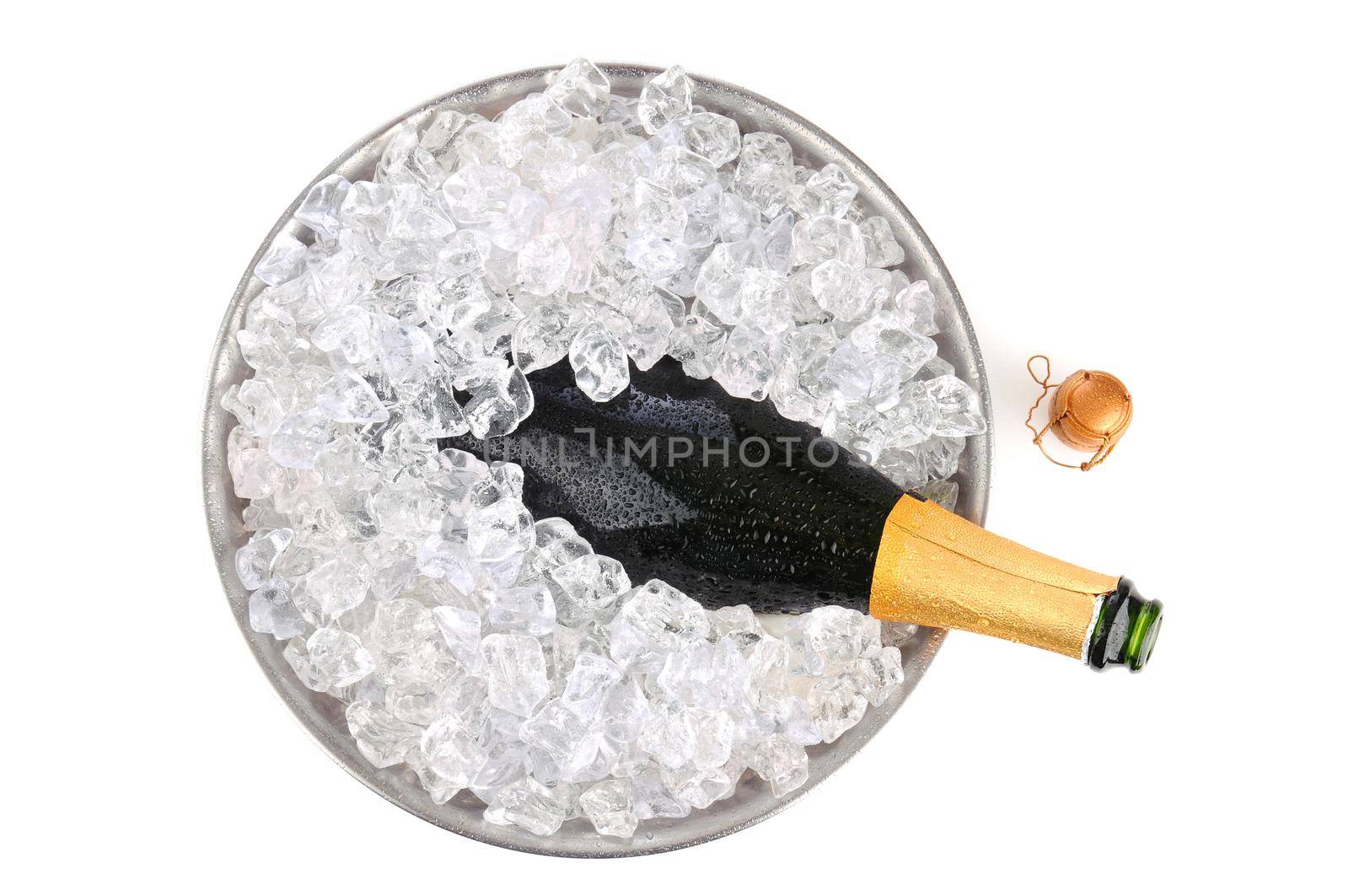 Overhead view of an open bottle of champagne in a metal ice bucket with condensation. Cork is on the  white background adjacent to the bottles neck.