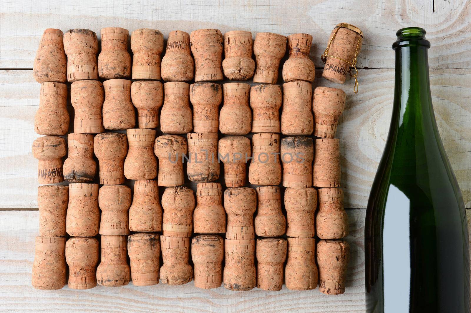 Overhead shot of a empty champagne bottle without label and corks. Closeup on a rustic white wood table. Horizontal format with copy space.