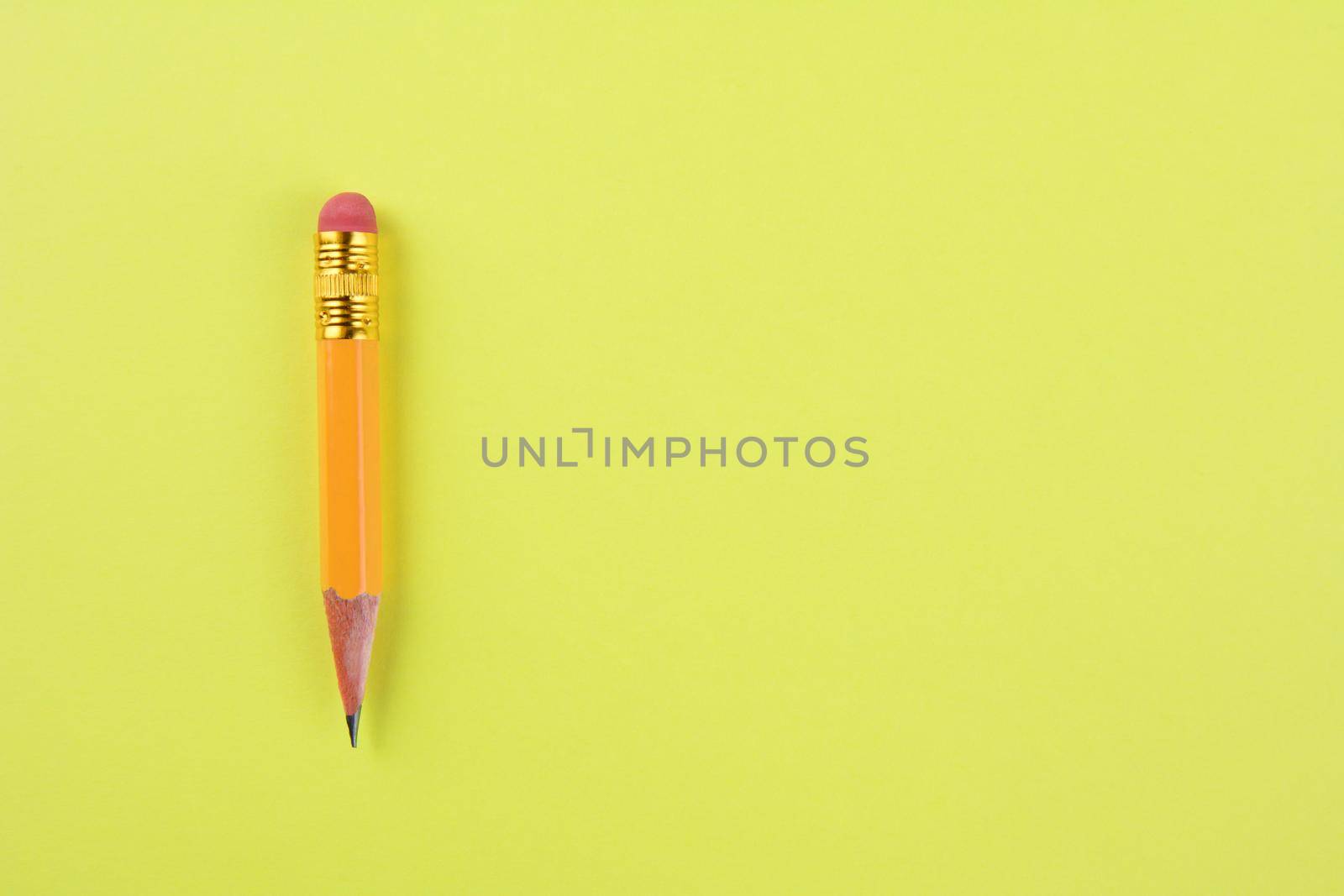 Overhead closeup of a sharpened pencil stub on a yellow background. The well used #2 pencil is set ot the left side of the frame, leaving copy space.