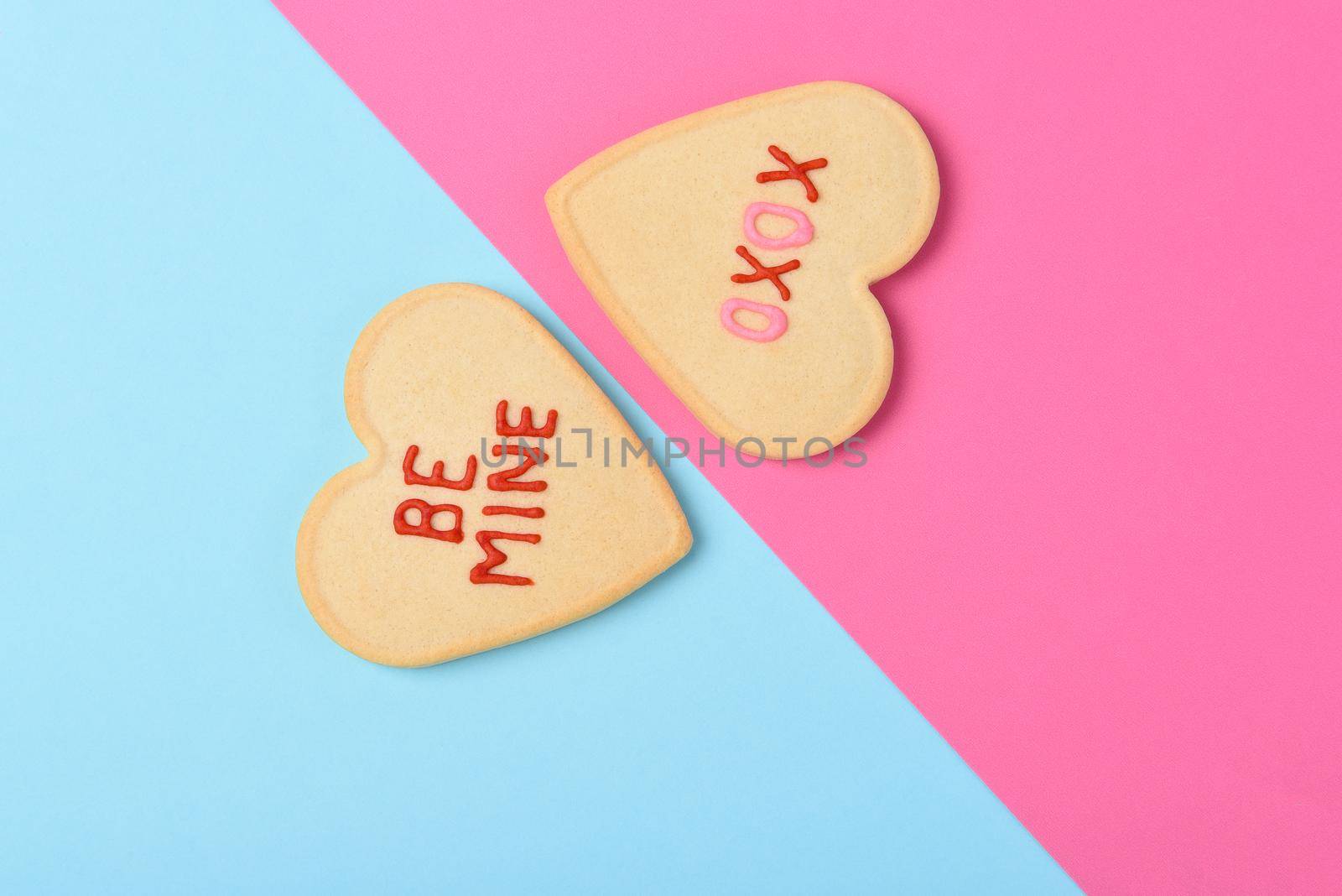 Valentines Day Concept: Two Heart shaped sugar cookies one on pink one on blue with Be Mine and XOXO written in icing.  by sCukrov