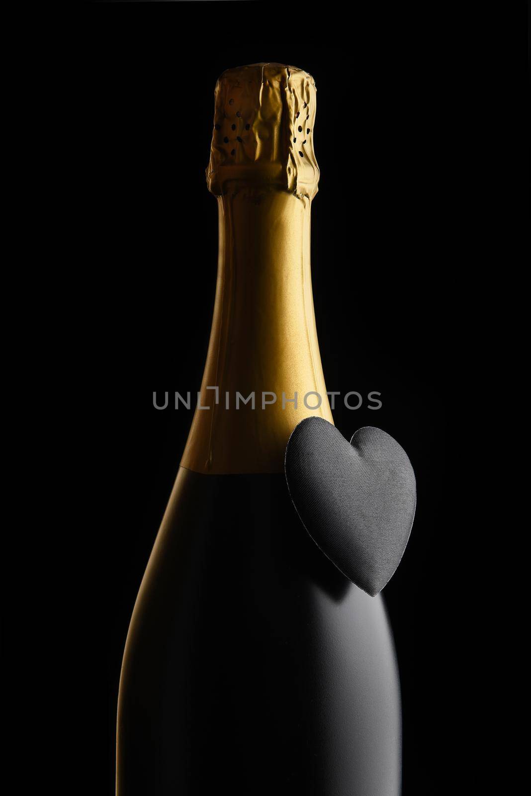 Valentines Day Concept: Closeup of a bottle of Champagne with a black heart against a black background.
