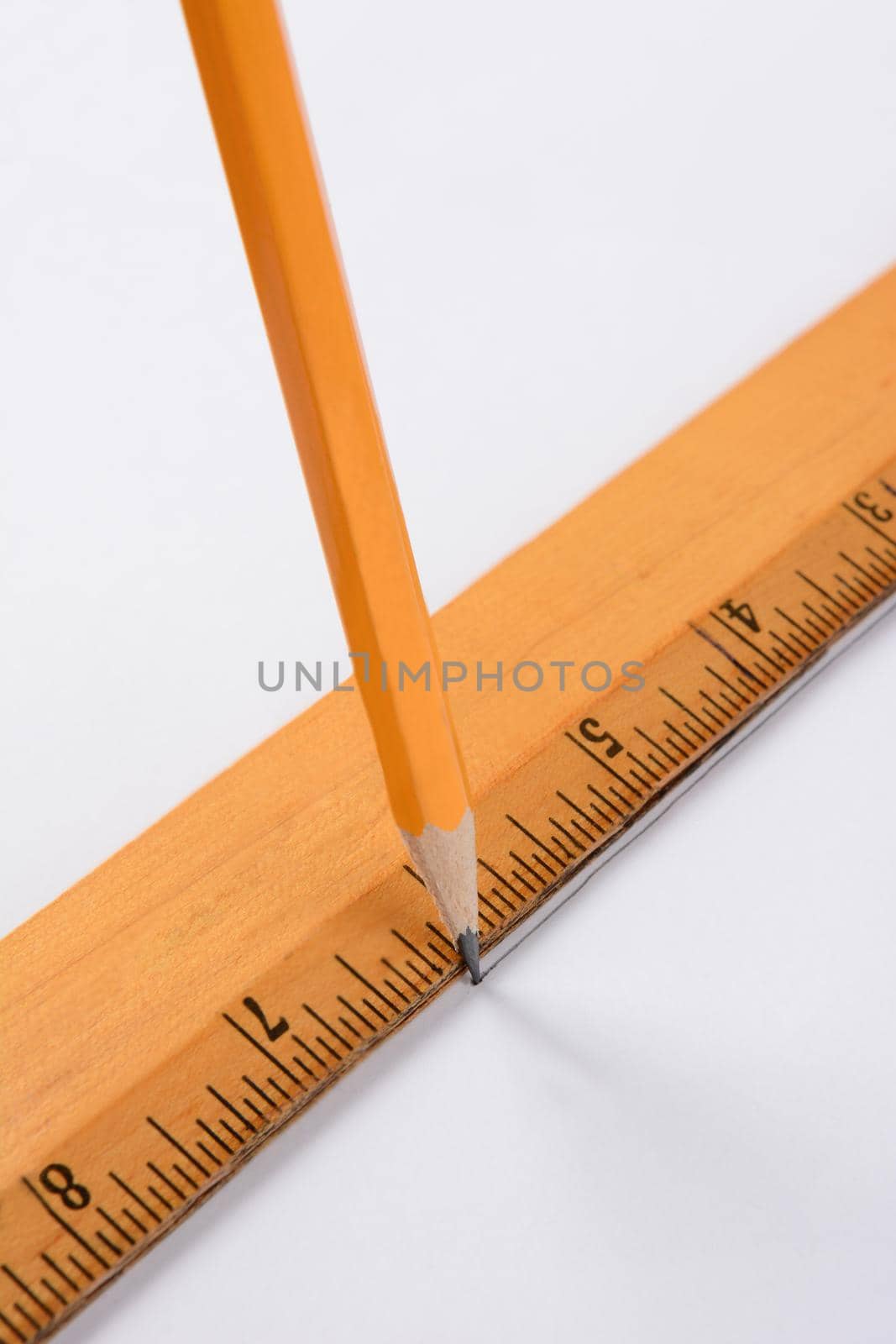A pencil and ruler drawing a line on a white sheet of paper. Closeup in vertical format.
