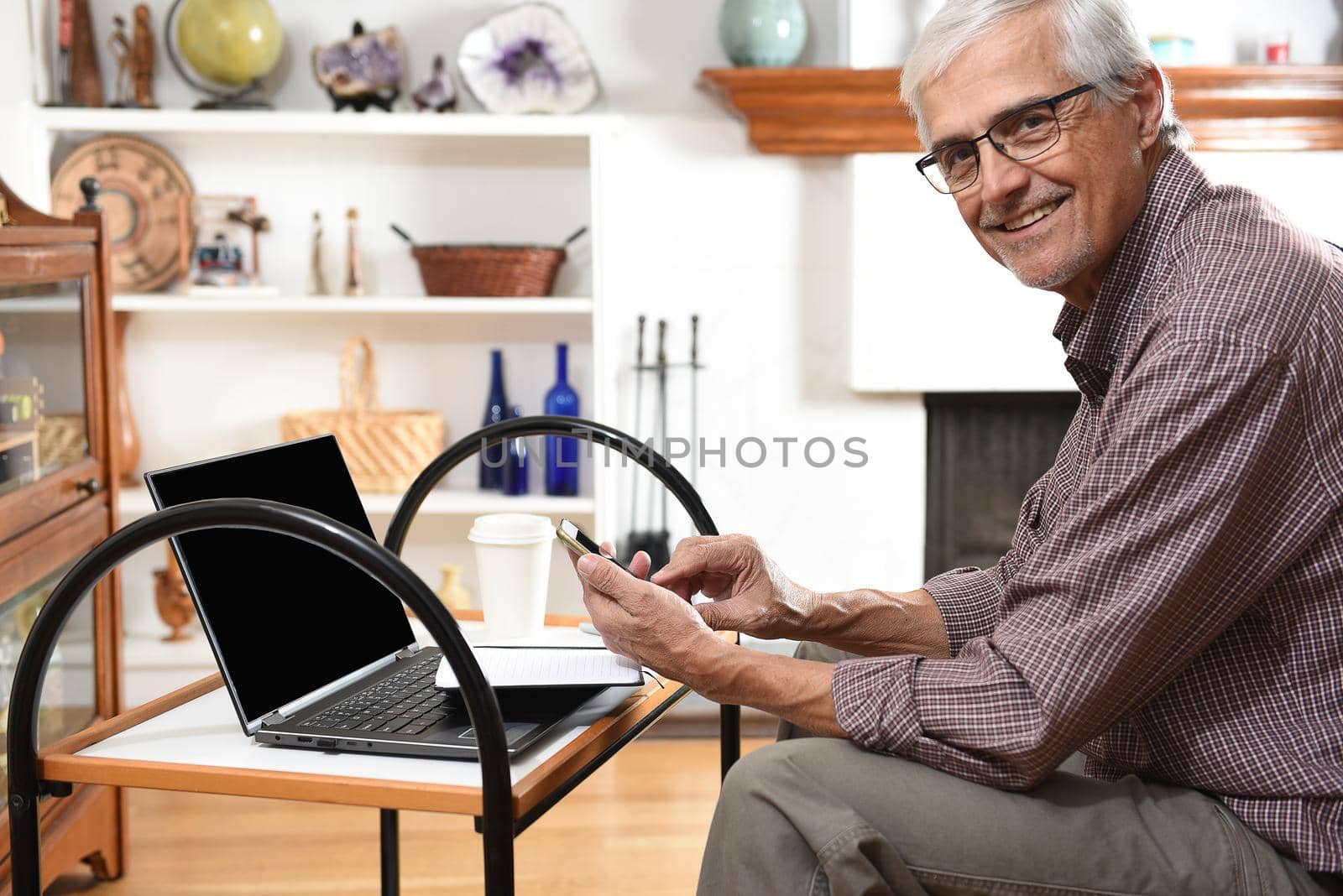 Mature man working from home with his laptop and cell phone. Man is looking at the samera ans smiling.