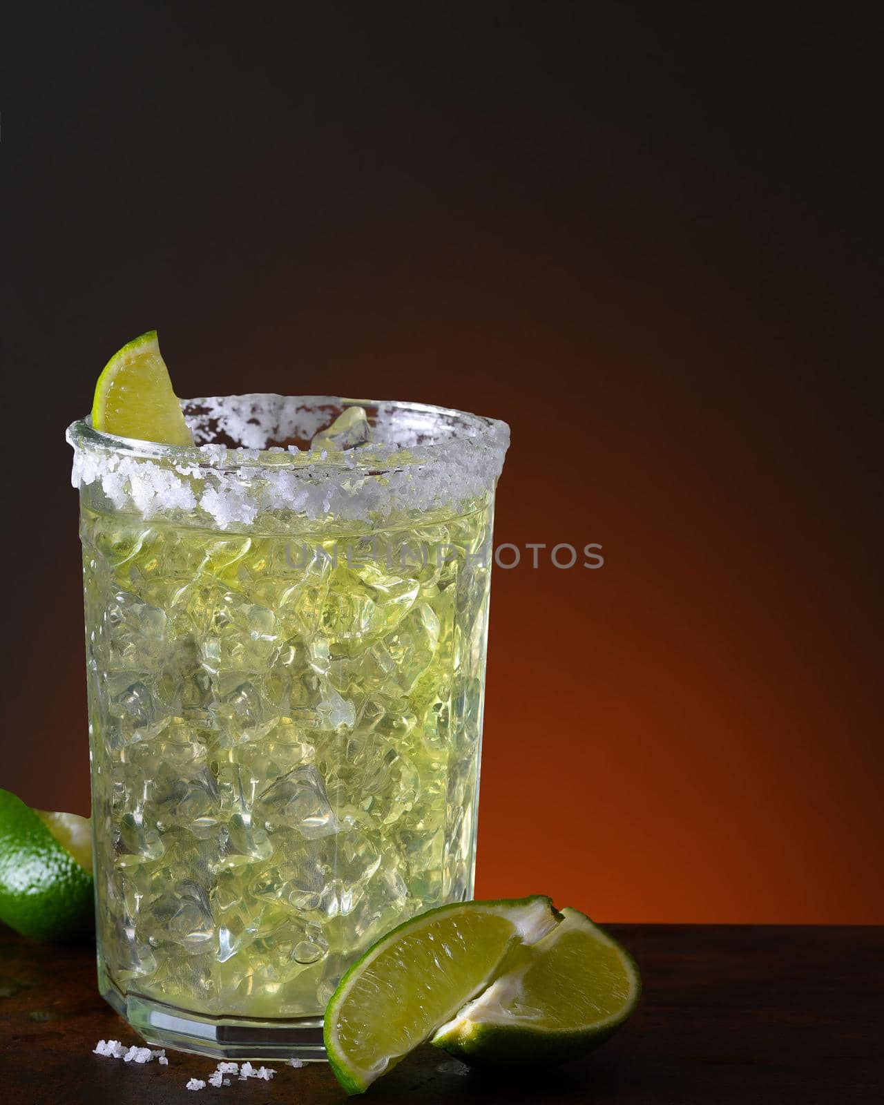 A margarita on the rocks in a glass tumbler. On a dark wood table with a warn light to dark background with copy space.