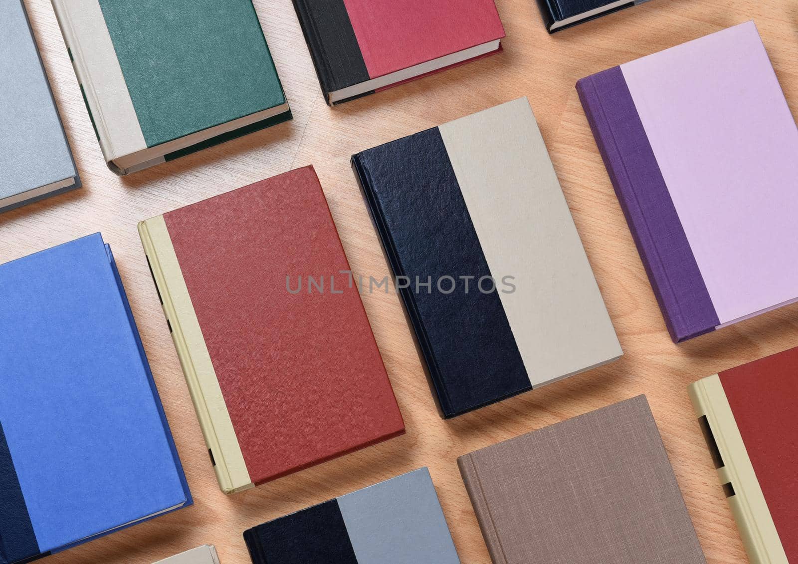 High angle view of rows of assorted text books laid out on a wood student desk. Closeup with the books at an angle.