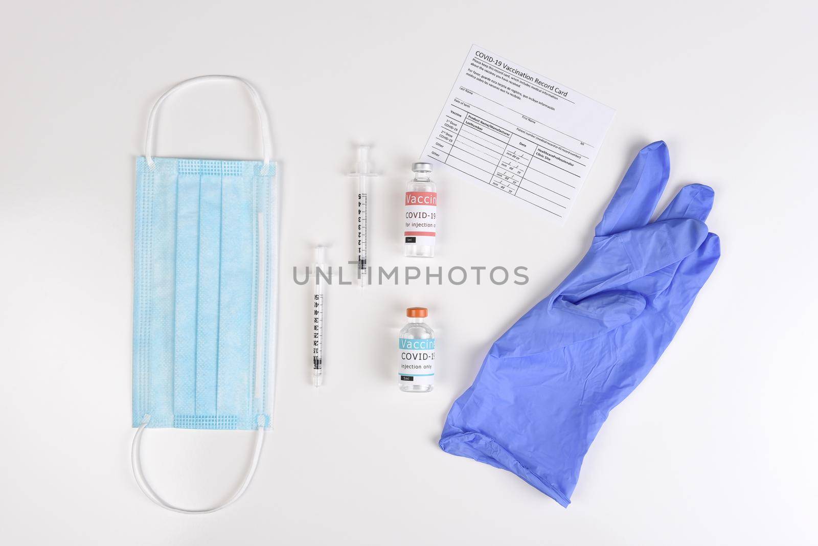 Equipment to administer a Covid19 Vaccination with record card. Flat lay with surgical mask, syringes, vaccine vials, and glove.
