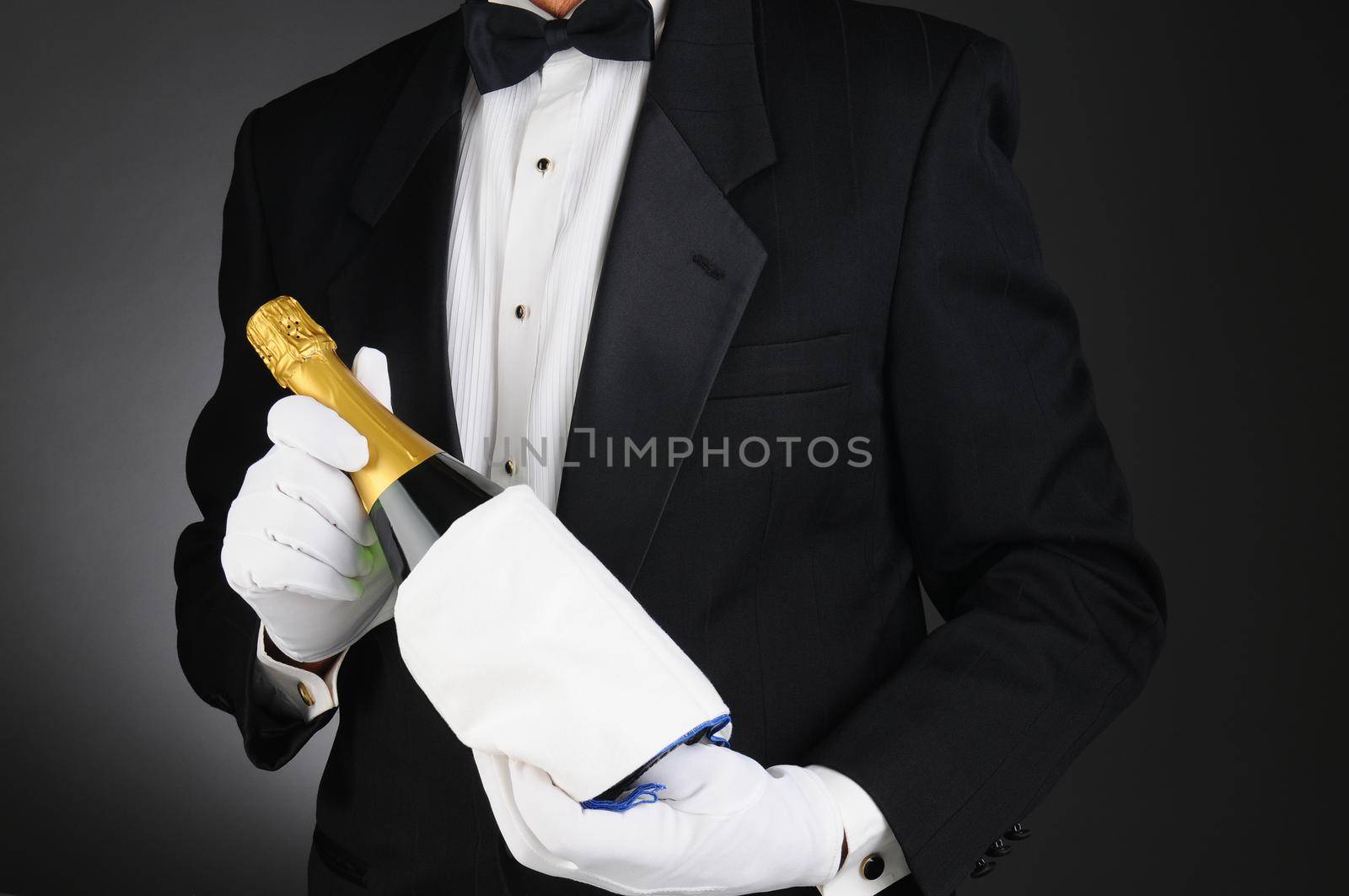 Closeup of a Sommelier holding a Champagne bottle in front of his torso. Man is unrecognizable. Horizontal format on a light to dark gray background.