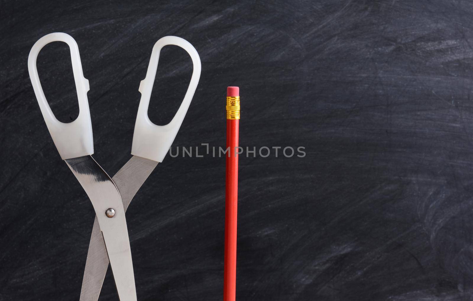 A red pencil and scissors standing in front of a chalkboard with eraser marks. Horizontal format with copy space. Back to School concept.