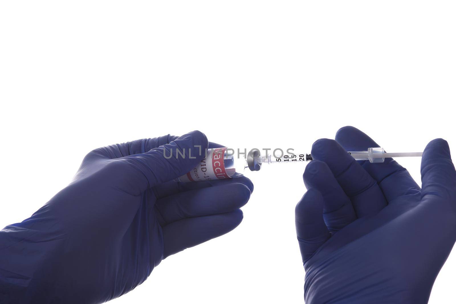 Closeup of two hands in surgical gloves with a syringe and vial of Covid-19 vaccine backlit over a white background. by sCukrov