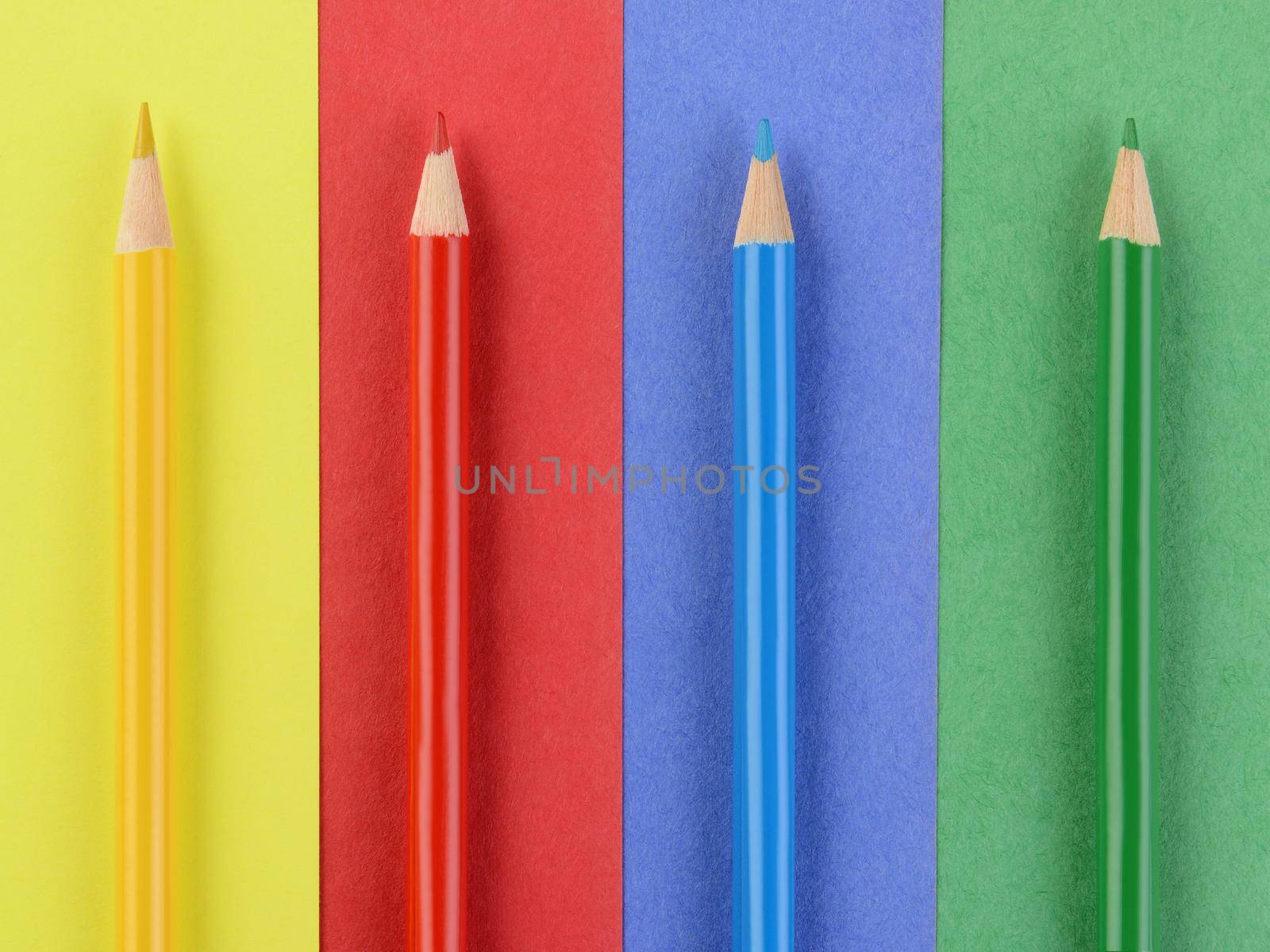 Overhead view of four colored pencils on matching colored paper. Closeup in horizontal format. Back to School concept.