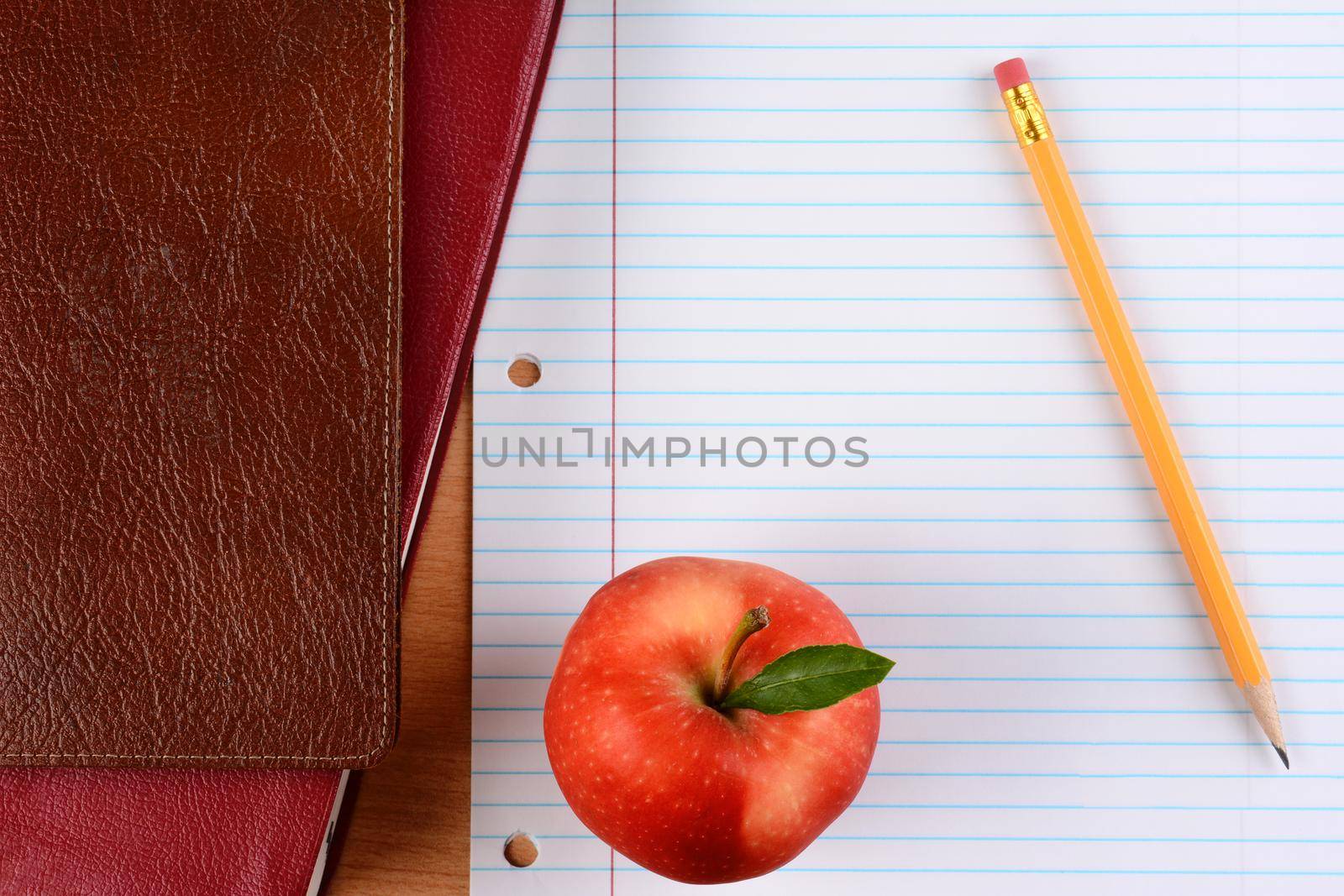 Overhead view of an apple  and pencil on notebook paper with school books. Closeup in horizontal format. Back to School concept.