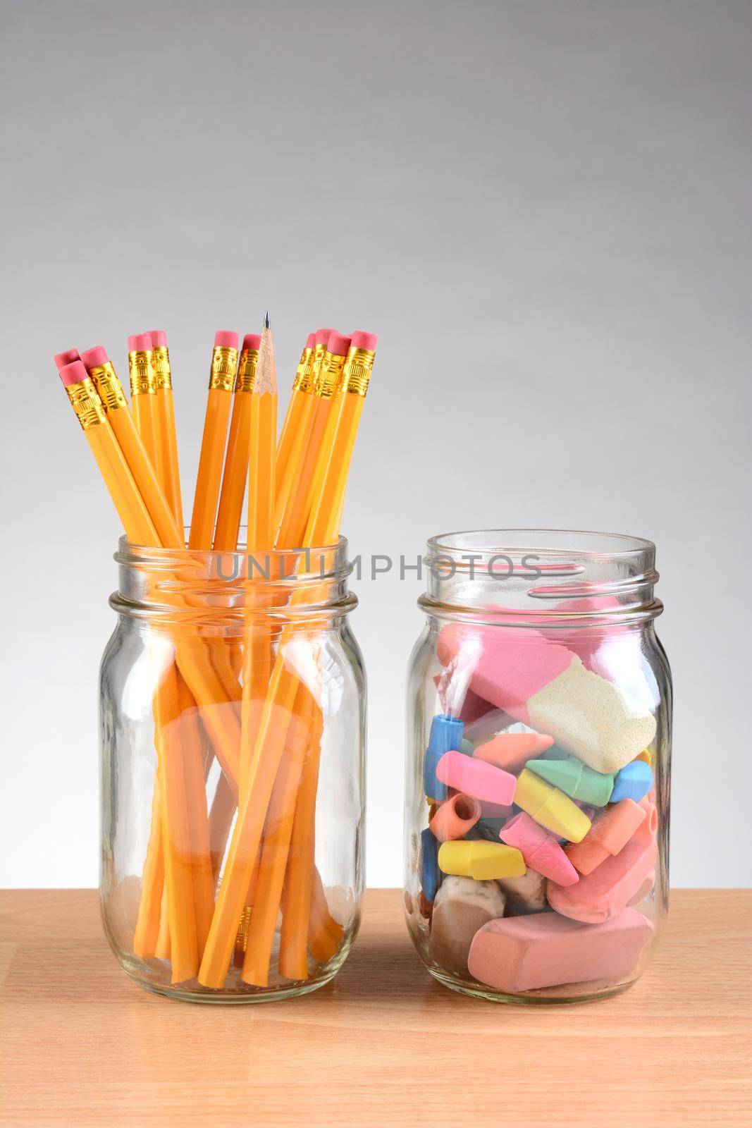 Closeup of two jars on a teachers desk with pencils and erasers. Vertical format on a light to dark gray background with copy space.