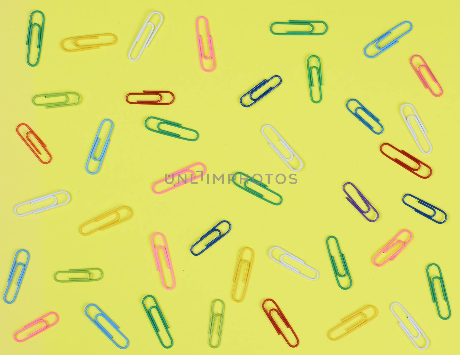 A group of multi-colored paper clips spread out on a yellow background.