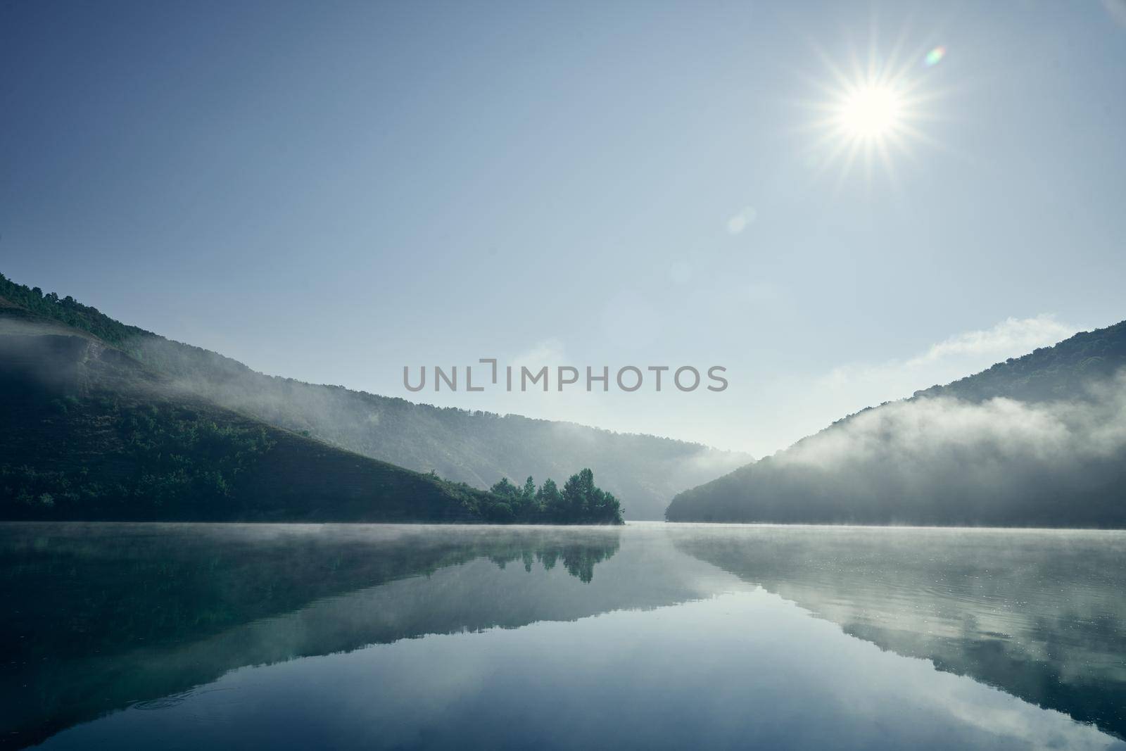 Morning landscape on river and hilly shores. Sunrise in mountains. Light fog rising above water. Mountains covering with forests. Still water.