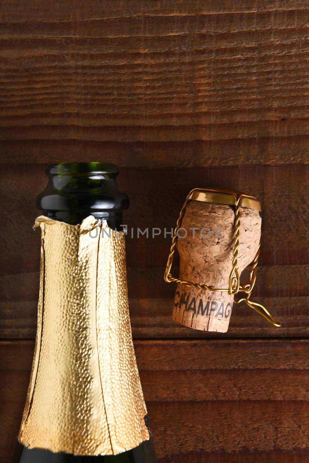 Top view of an opened Champagne bottle next to a cork and cage. Vertical format on dark wood background, with copy space.