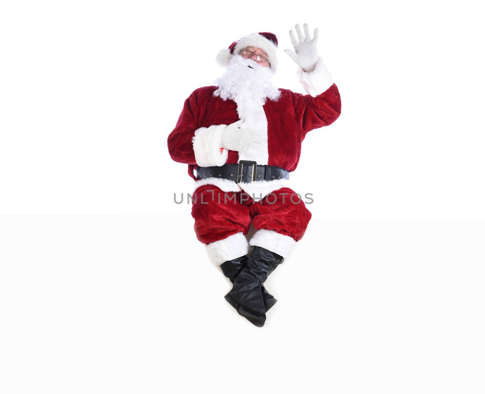 Senior man in traditional Santa Claus Suit sitting on a white wall with one hand in the air and the other on his belly and his eyes closed. by sCukrov