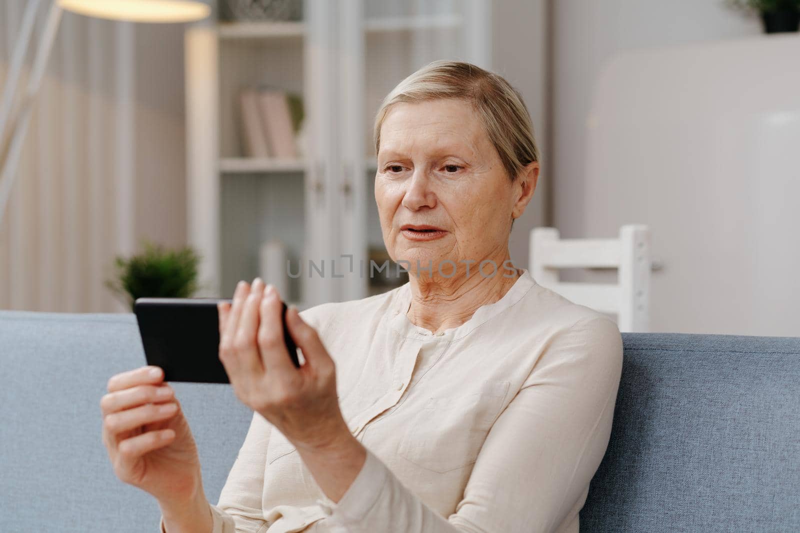 mature woman with a smartphone sitting on the couch. by SmartPhotoLab