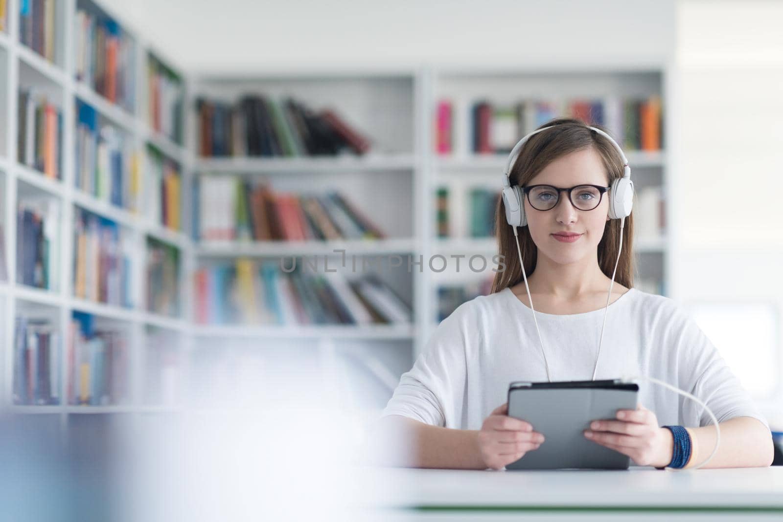 female student study in school library, using tablet and searching for information’s on internet. Listening music and lessons on white headphones