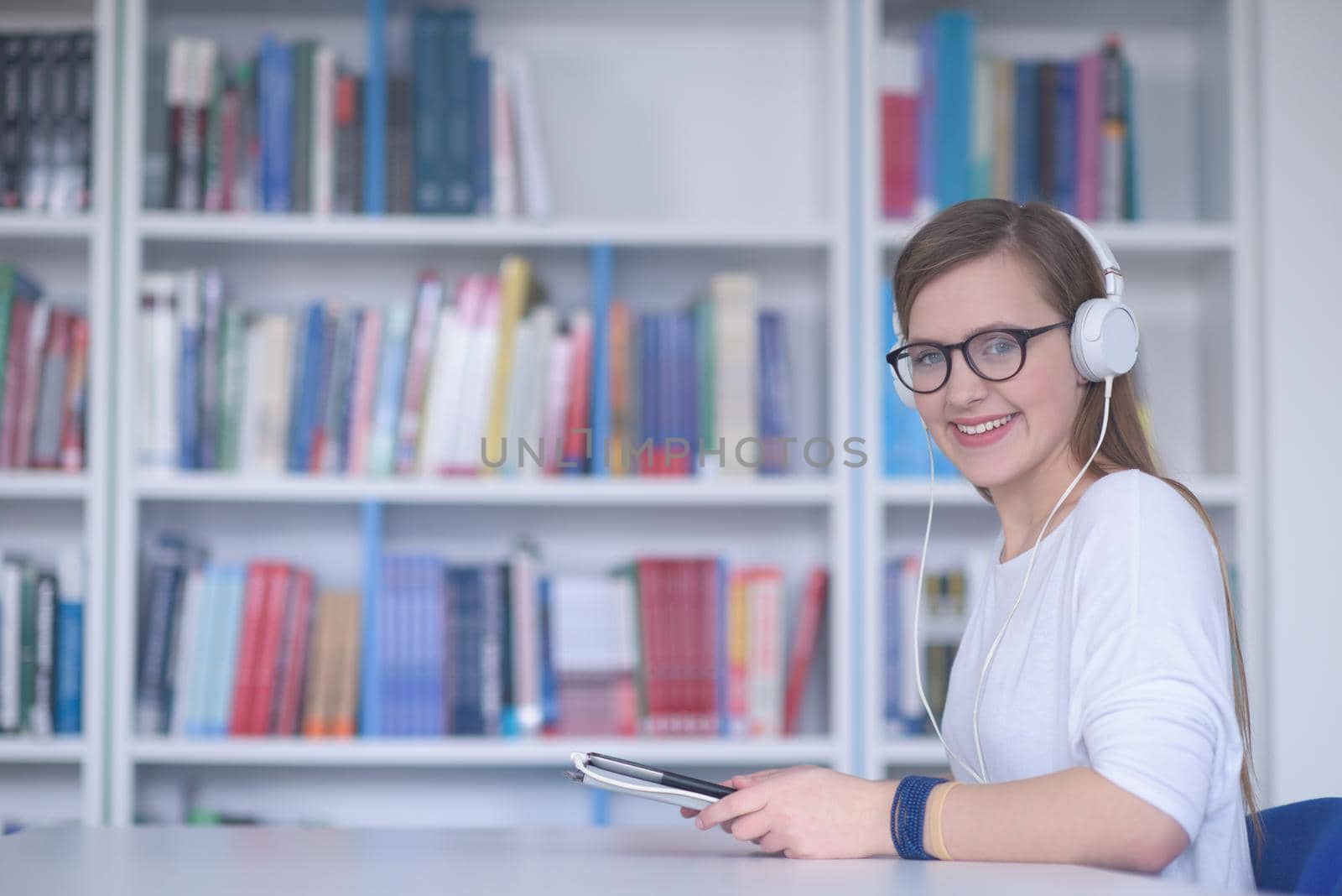 female student study in school library, using tablet and searching for information’s on internet. Listening music and lessons on white headphones