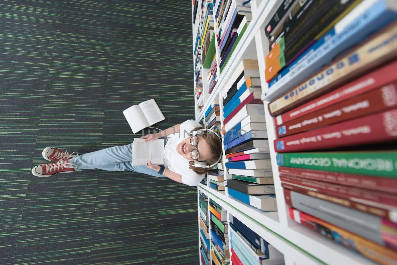 female student study in school library, using tablet and searching for information’s on internet. Listening music and lessons on white headphones