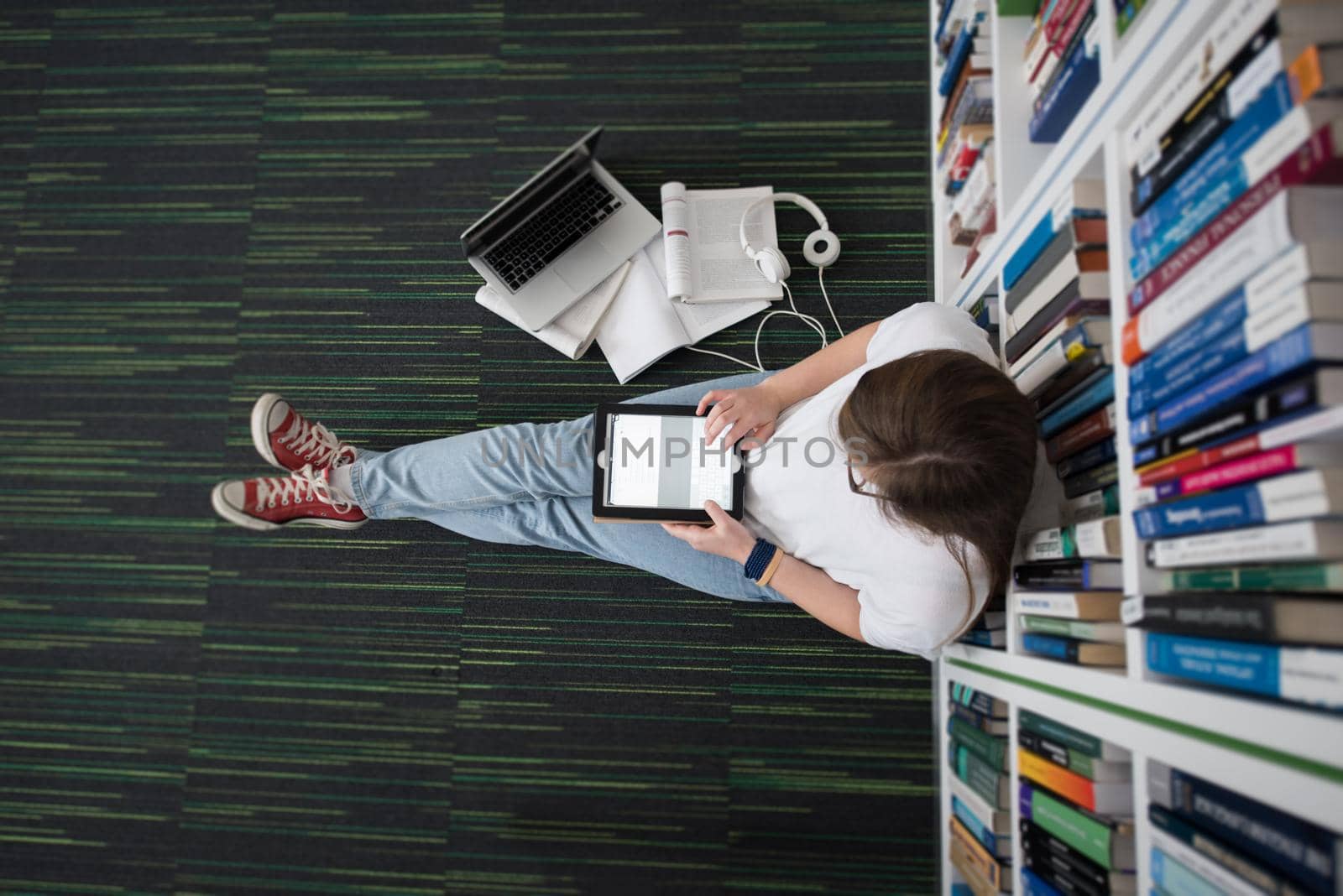 female student study in school library, using tablet and searching for information’s on internet. Listening music and lessons on white headphones