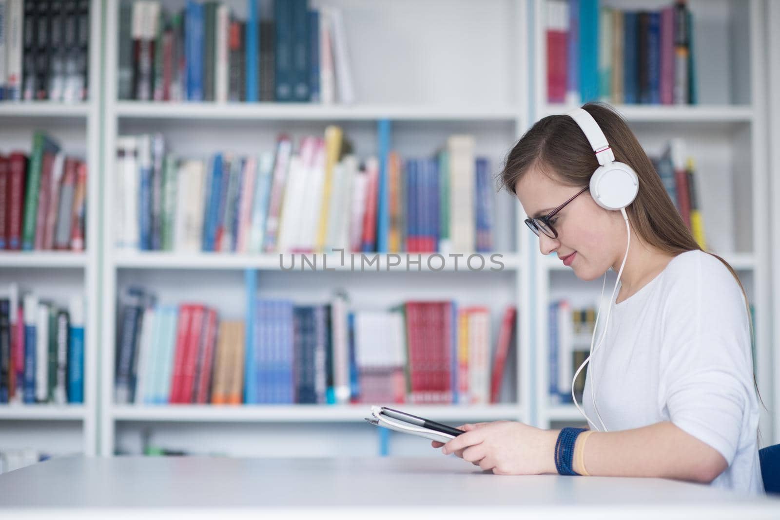 female student study in school library, using tablet and searching for information’s on internet. Listening music and lessons on white headphones