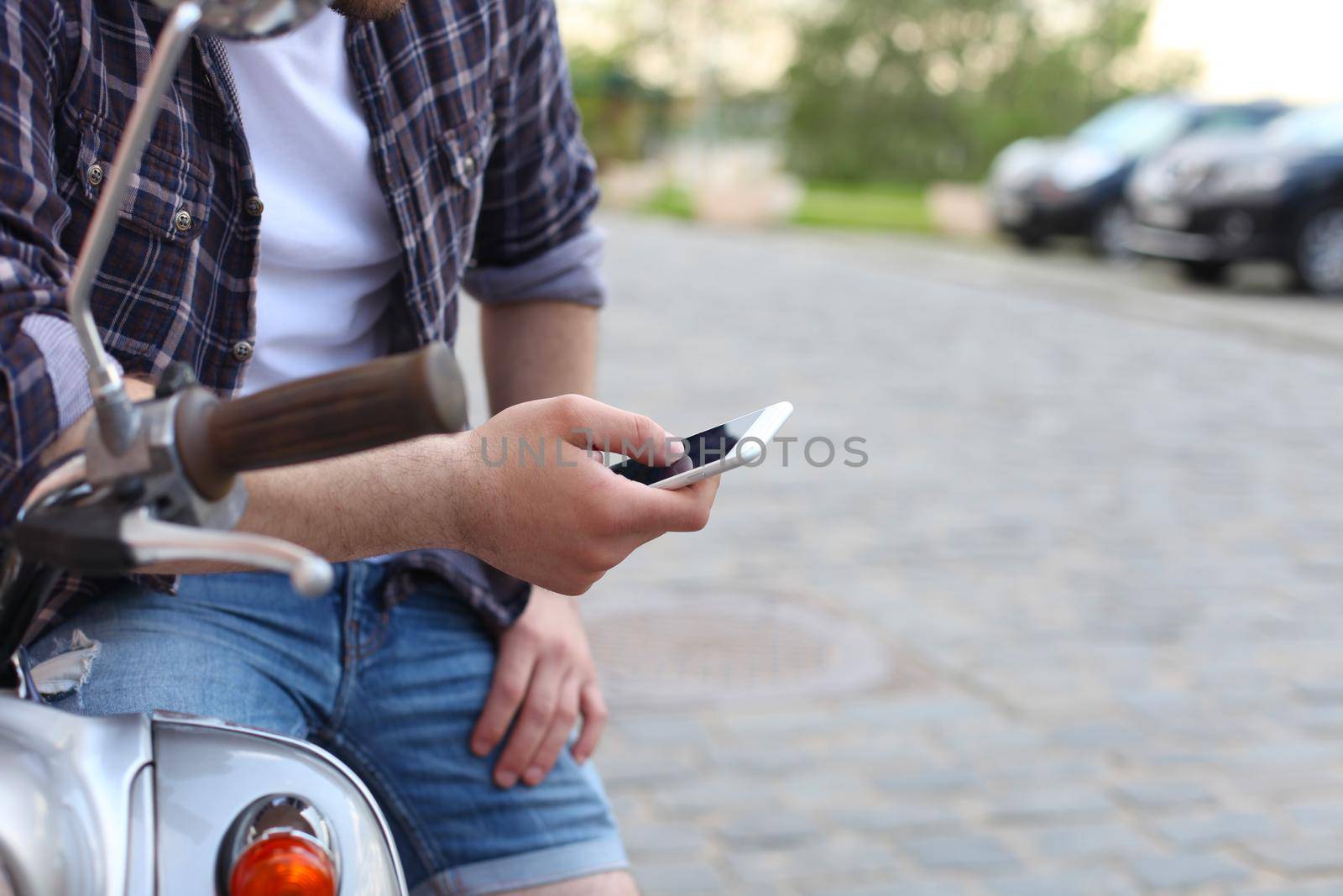 Young man sitting on scooter and using smart phone