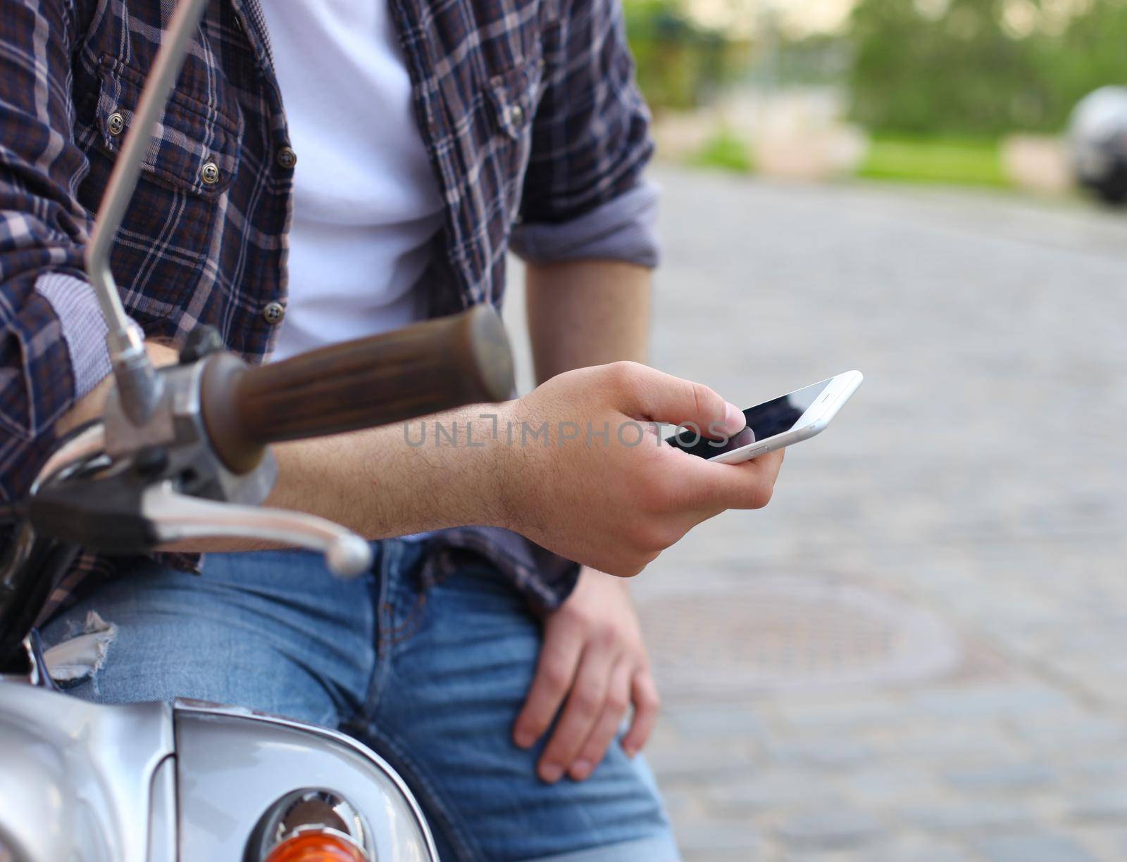 Young man sitting on scooter and using smart phone