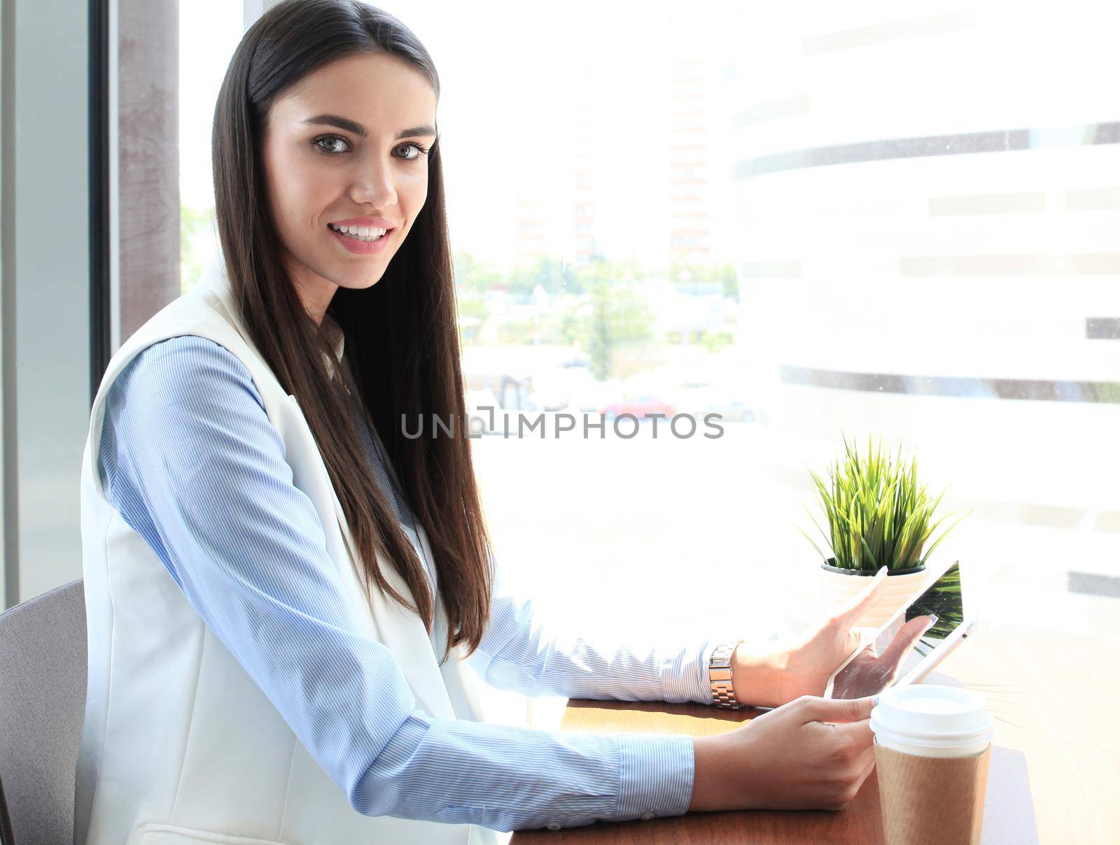 Modern businesswoman drinking coffee in the office cafe during lunch time and using tablet