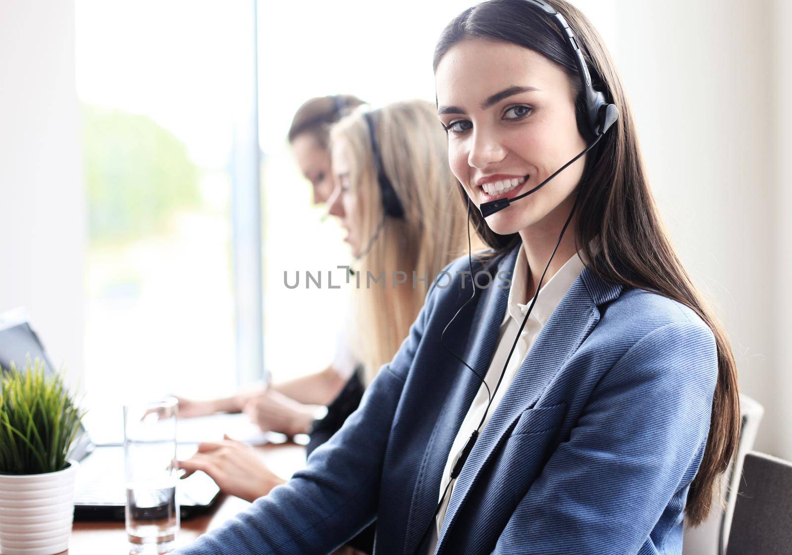 Portrait of call center worker accompanied by her team. Smiling customer support operator at work. by tsyhun