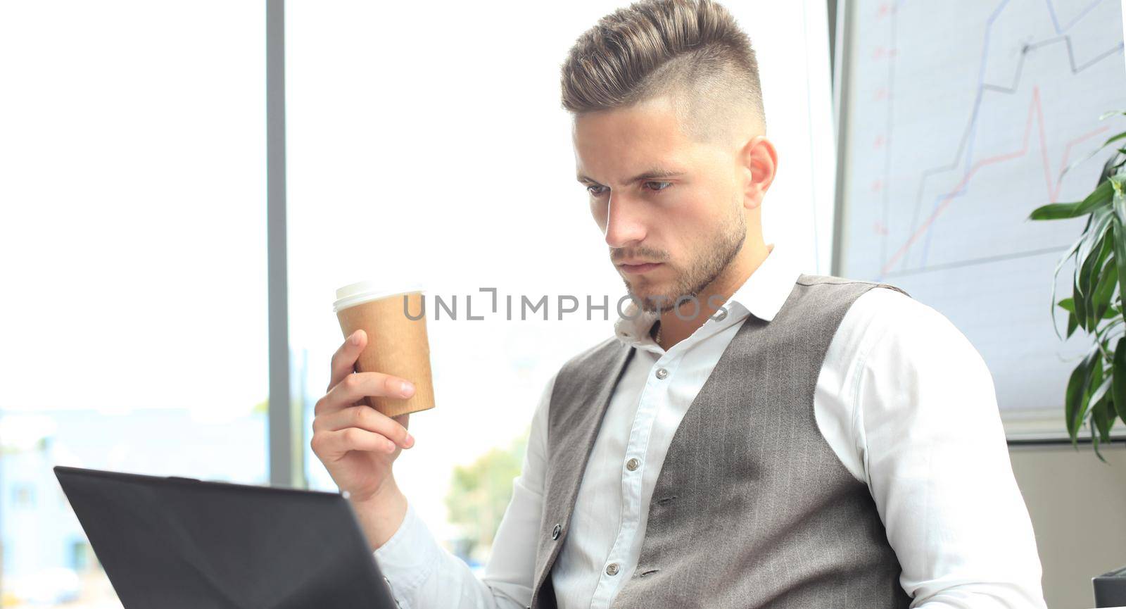 Modern businessman drinking coffee in the office cafe during lunch time and using laptop