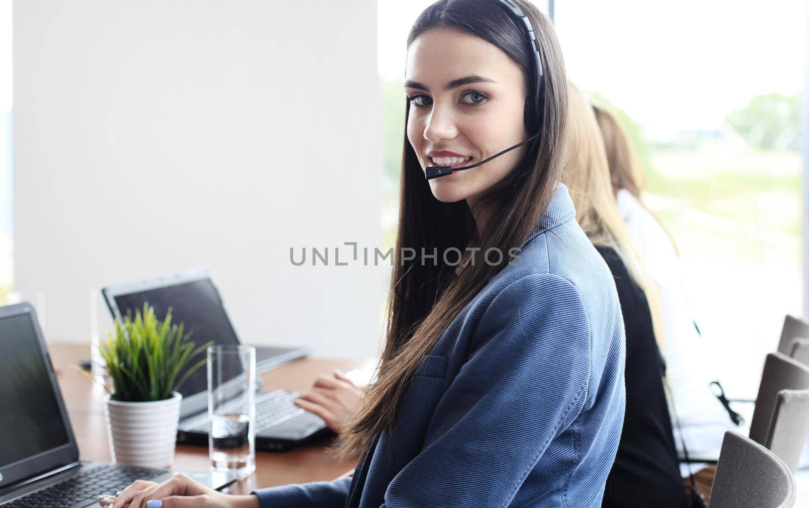 Portrait of call center worker accompanied by her team. Smiling customer support operator at work.