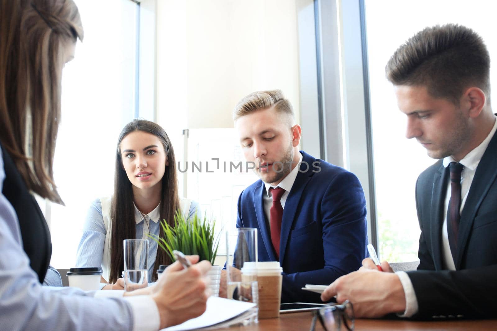 Young handsome man gesturing and discussing something while his coworkers listening to him sitting at the office table