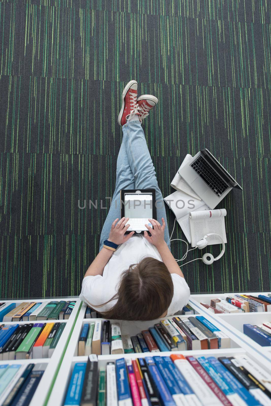 female student study in school library, using tablet and searching for information’s on internet. Listening music and lessons on white headphones