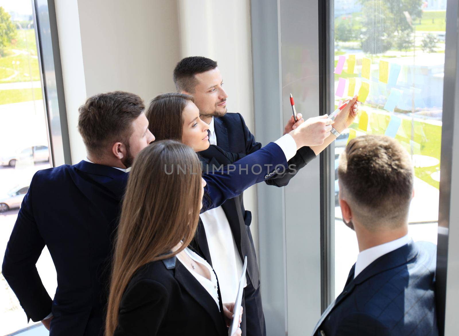 young creative startup business people on meeting at modern office making plans and projects with post stickers on glass by tsyhun