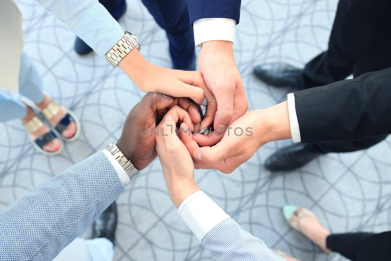 Multiethnic group of young people putting their hands on top of each other. Close up image of young business people making a stack of hands. by tsyhun