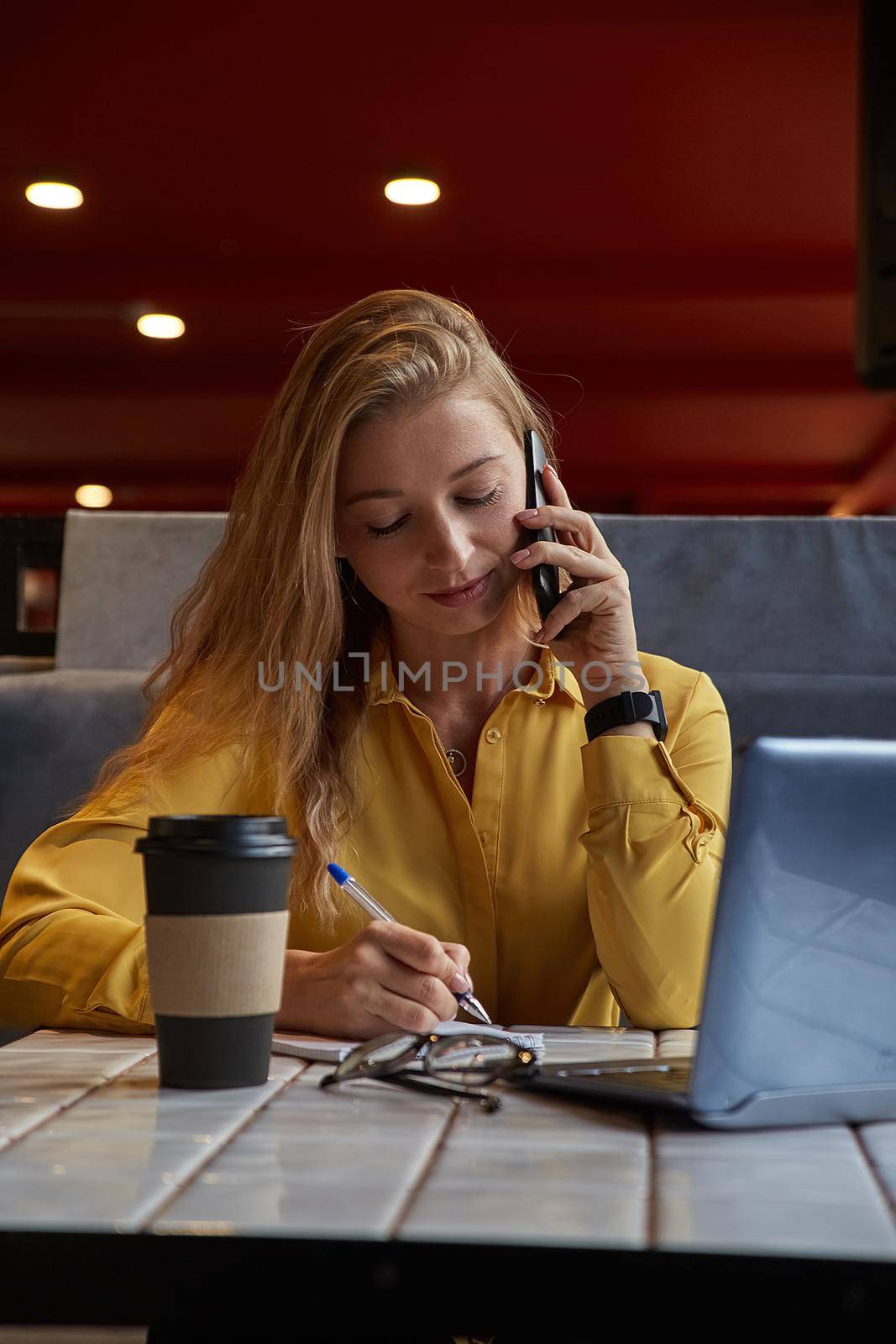 young attractive blond cauasian woman sitting at coffe shop, working on laptop by artemzatsepilin