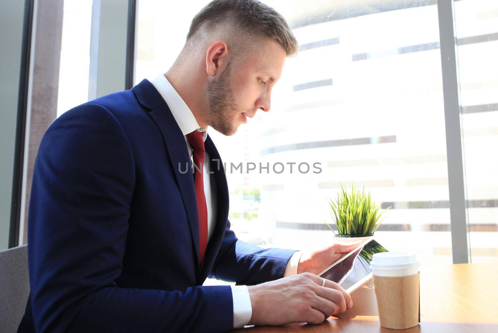Modern businessman drinking coffee in the office cafe during lunch time and using tablet