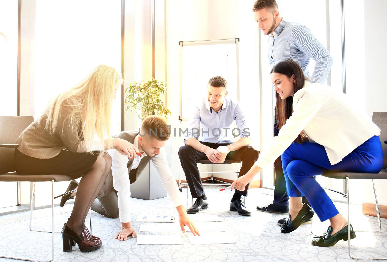 Creative people looking at project plan laid out on floor. Business associates discussing project plan in modern office.