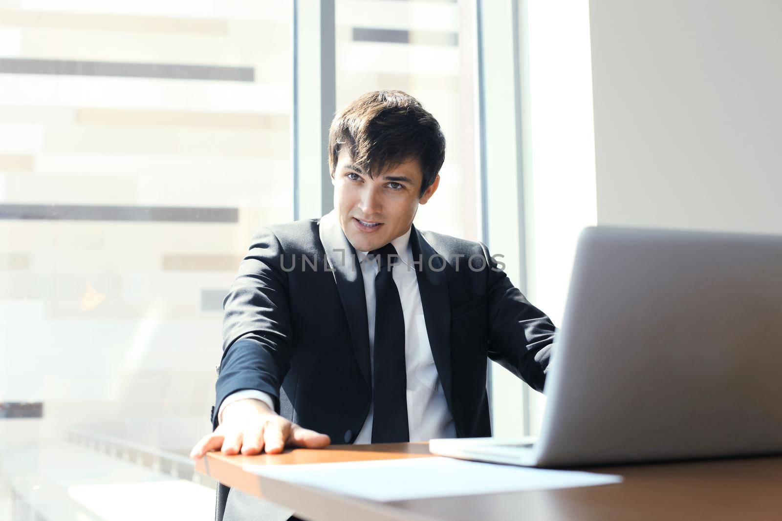 Portrait of happy businessman sitting at office desk, looking at camera, smiling. by tsyhun