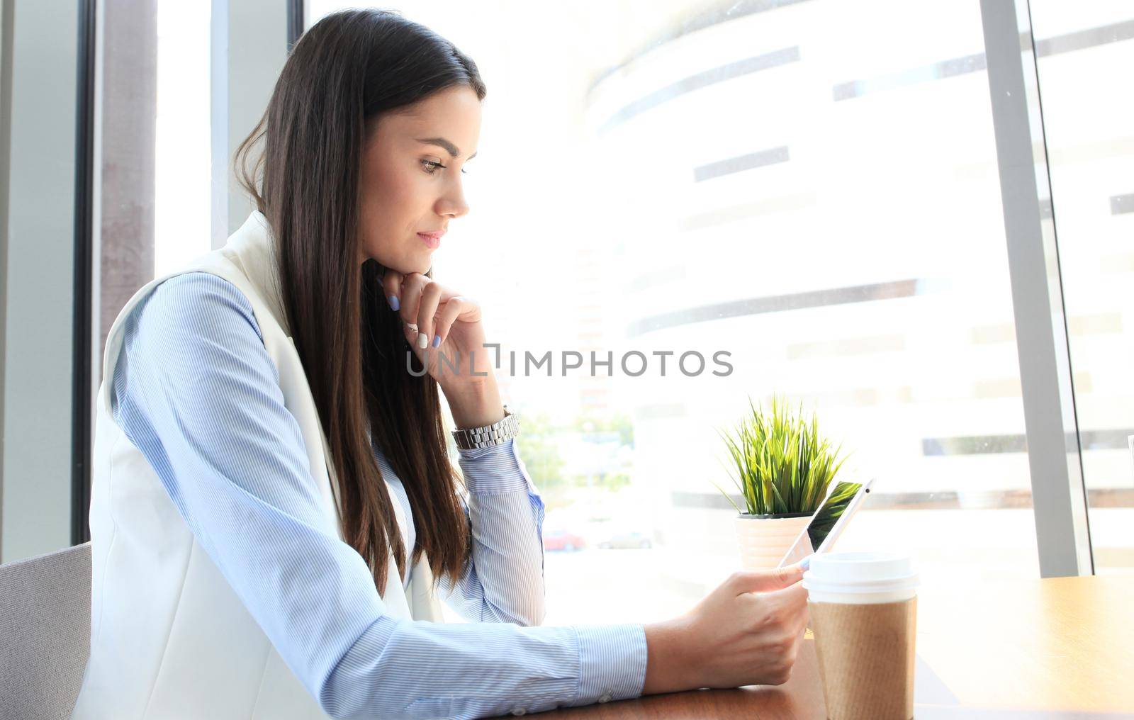 Modern businesswoman drinking coffee in the office cafe during lunch time and using tablet by tsyhun