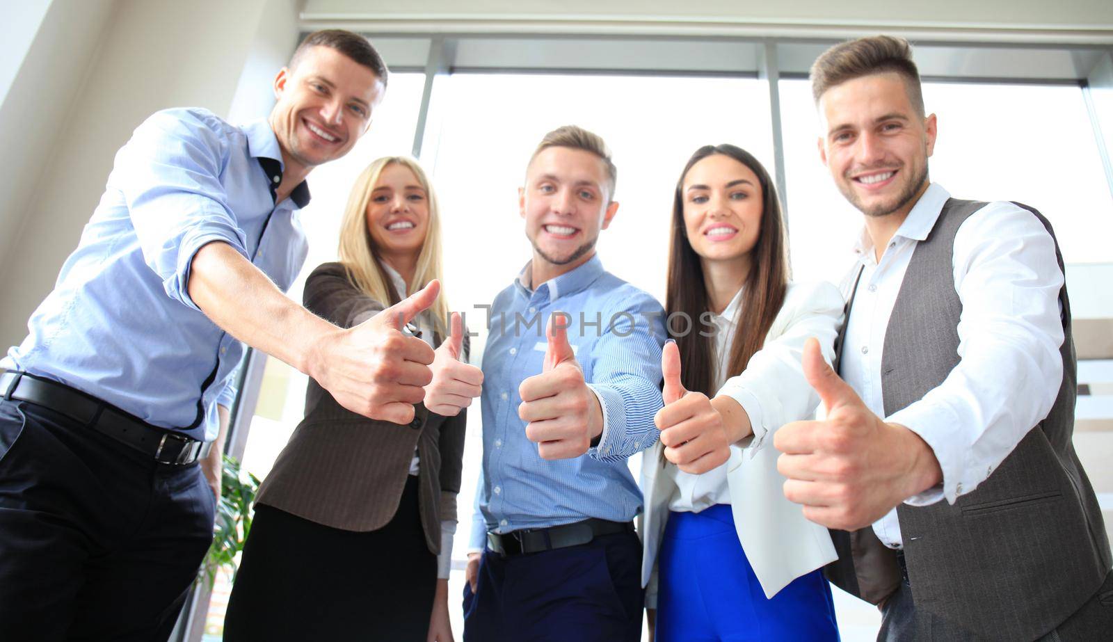 Portrait of happy businesspeople standing in office showing thumb up by tsyhun