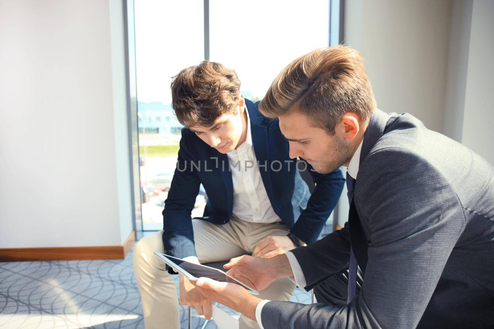 Mature businessman using a digital tablet to discuss information with a younger colleague in a modern business office.