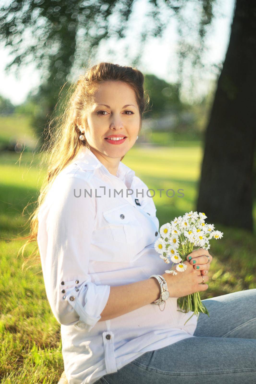 Beautiful pregnant woman relaxing outside in the park with flowers camomile in the hands
