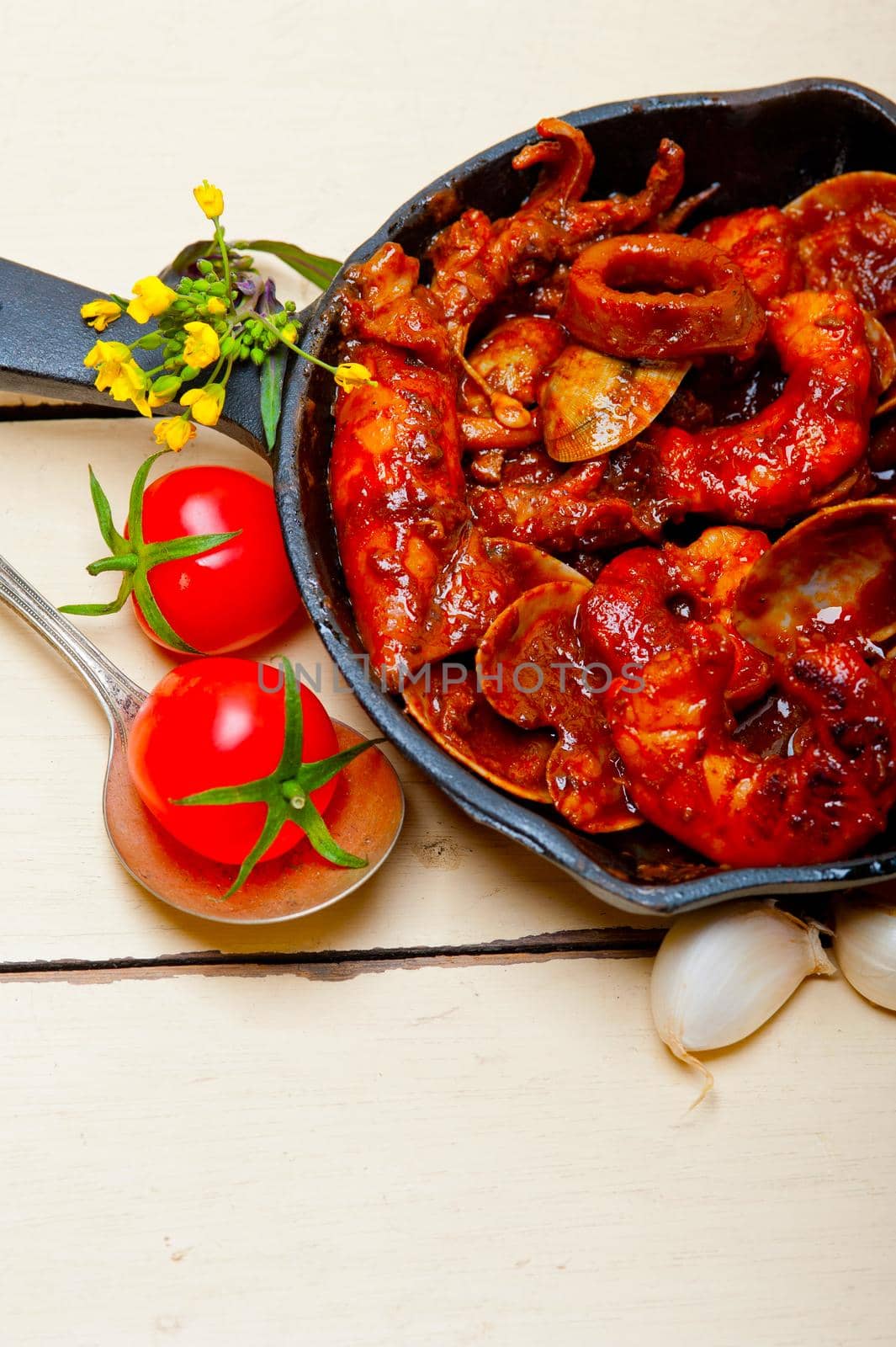 fresh seafood stew prepared on an iron skillet ove white rustic wood table 