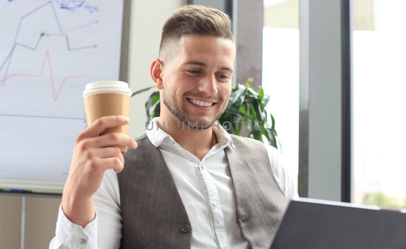 Modern businessman drinking coffee in the office cafe during lunch time and using laptop