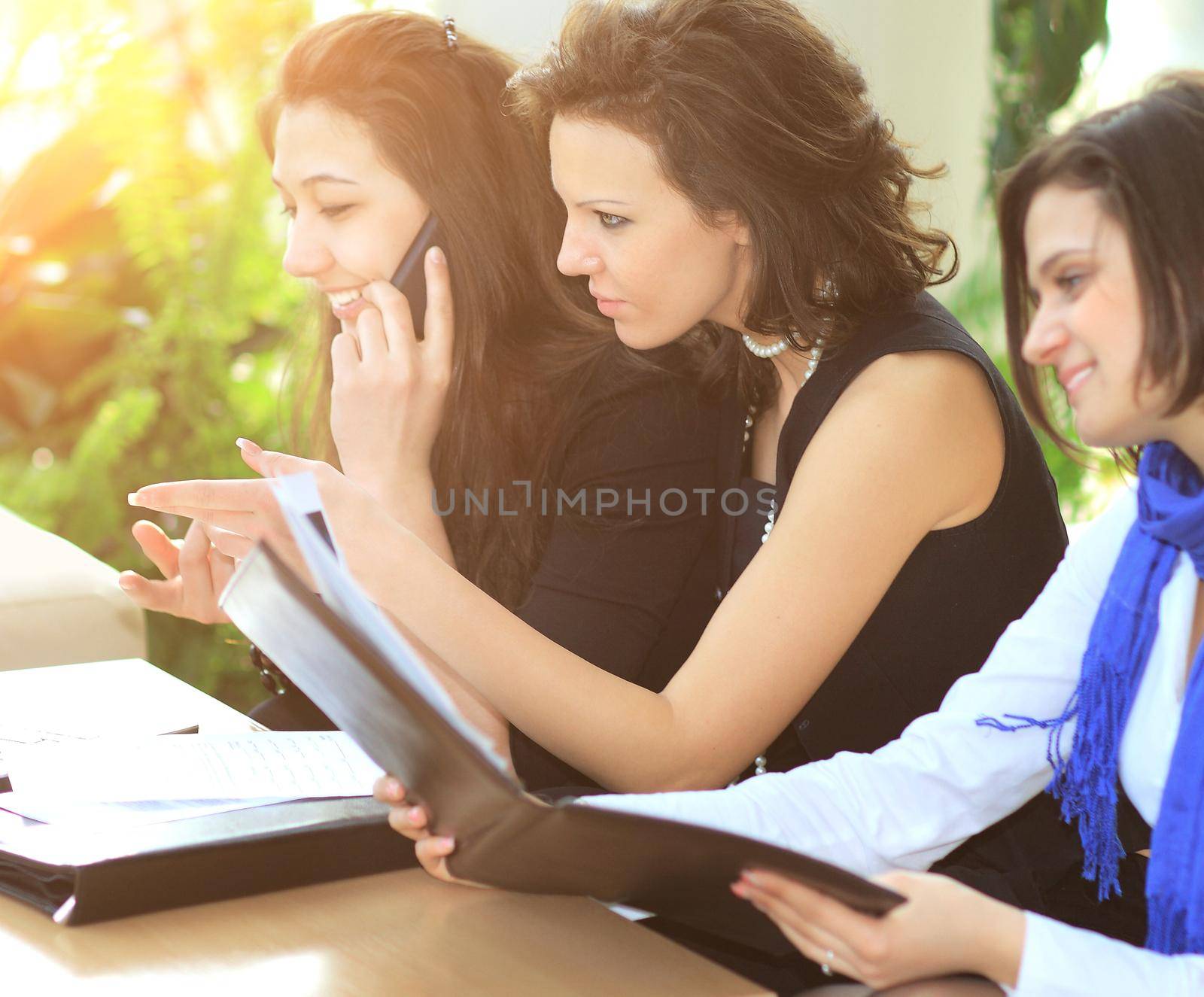 cheerful group of managers discussing work, looking at laptop screen, examining important documents and talking on the phone