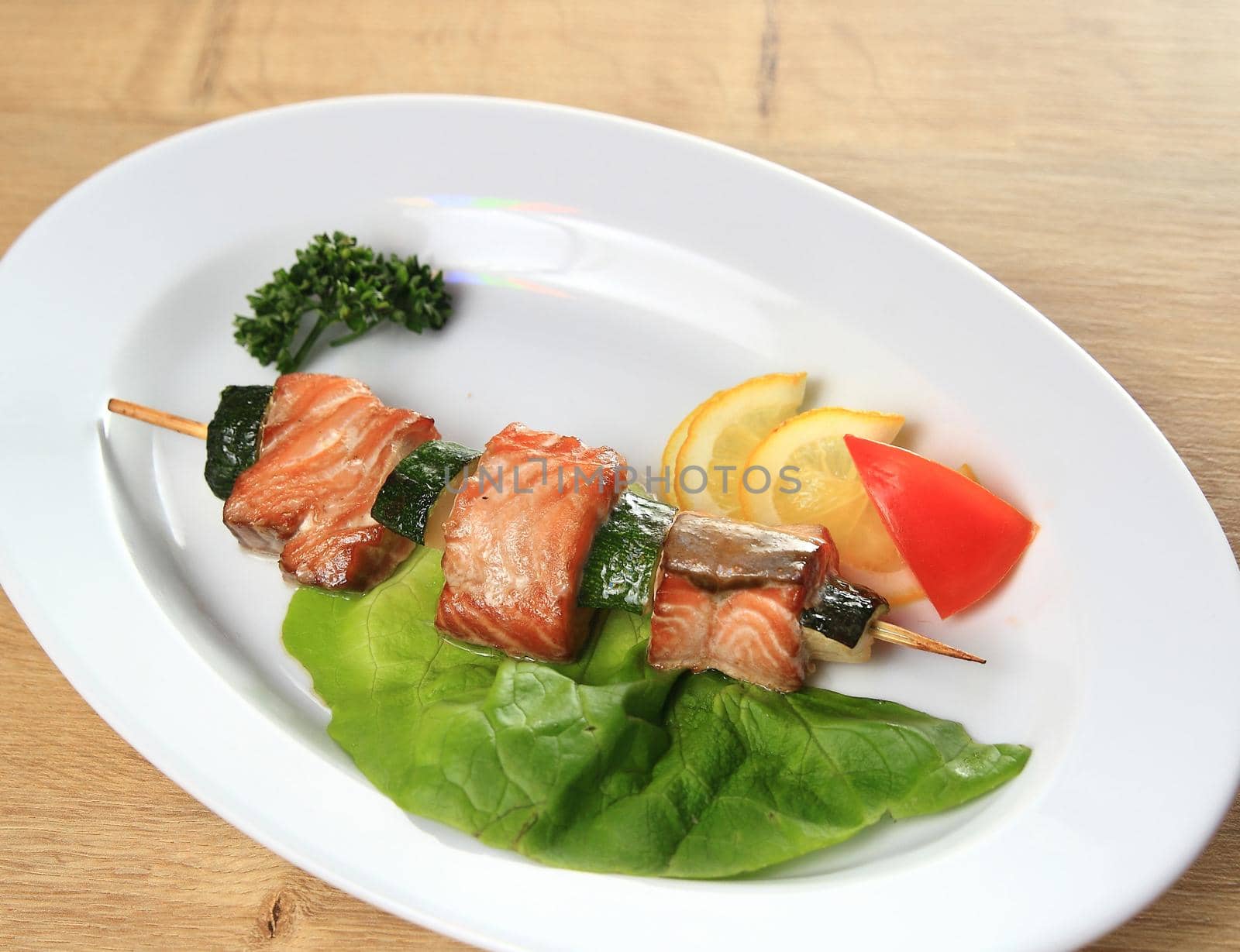 skewers of salmon with garnish on white plate on wooden backgrou